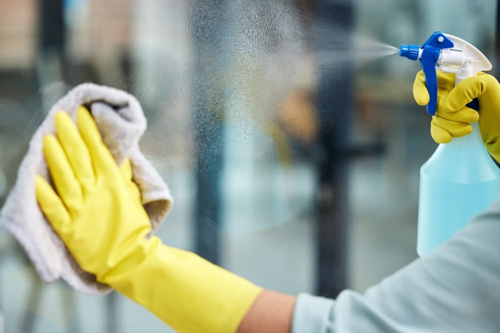 Reinigungskraft mit Handschuhen reinigt Fenster